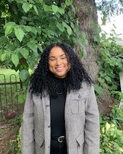 Jessina Emmert standing outdoors smiling, with tree and foliage in the background