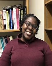 Agnes Phoebe Muyanga standing in front of a bookshelf full of books, smiling